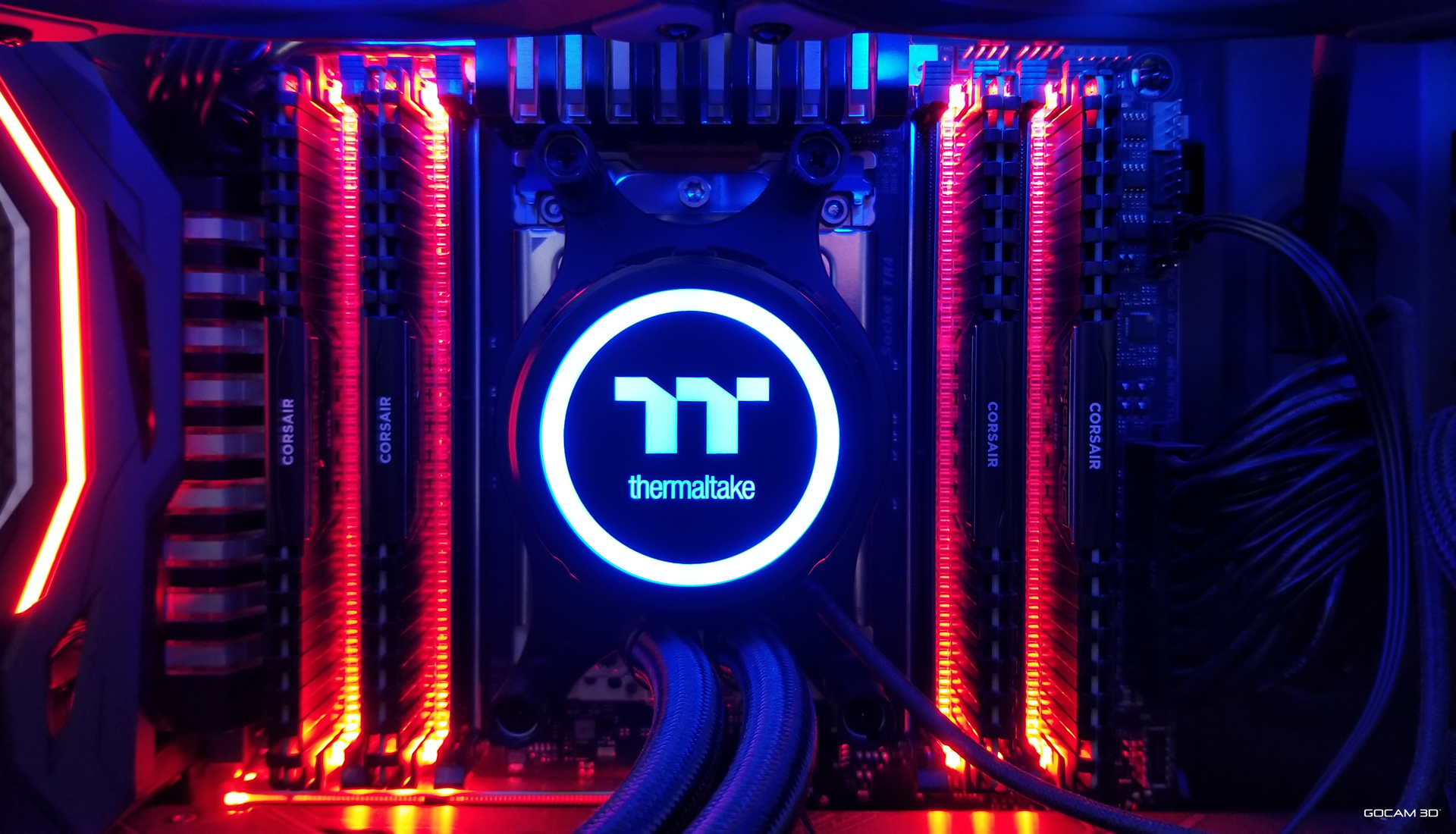 Gros plan sur l'intérieur d'une station de travail GOCAM 3D haute performance rétroéclairée de bleu et de rouge. On y voit un refroidisseur liquide Thermaltake circulaire lumineux installé sur un processeur AMD Threadripper 2990wx, entouré de barrettes de mémoire vive Corsair de chaque côté.